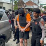 Salah seorang tersangka pembunuhan warga negara Australia saat melakukan reka ulang dikawal ketat oleh pasukan dari Satuan Brimob Polda Bali dengan tangan diborgol, Rabu (30/7/2025). (Foto: ist)